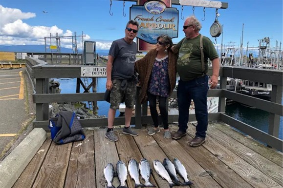 Guests from Bayside Oceanfront Resort holding freshly caught Coho salmon aboard French Creek Fishing